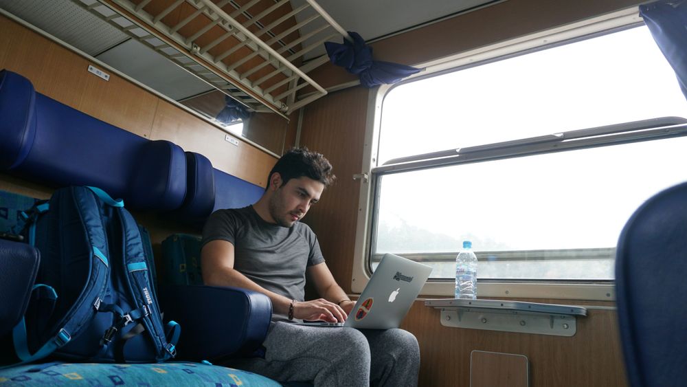 A man working on a computer in a train representing the travel for a living concept