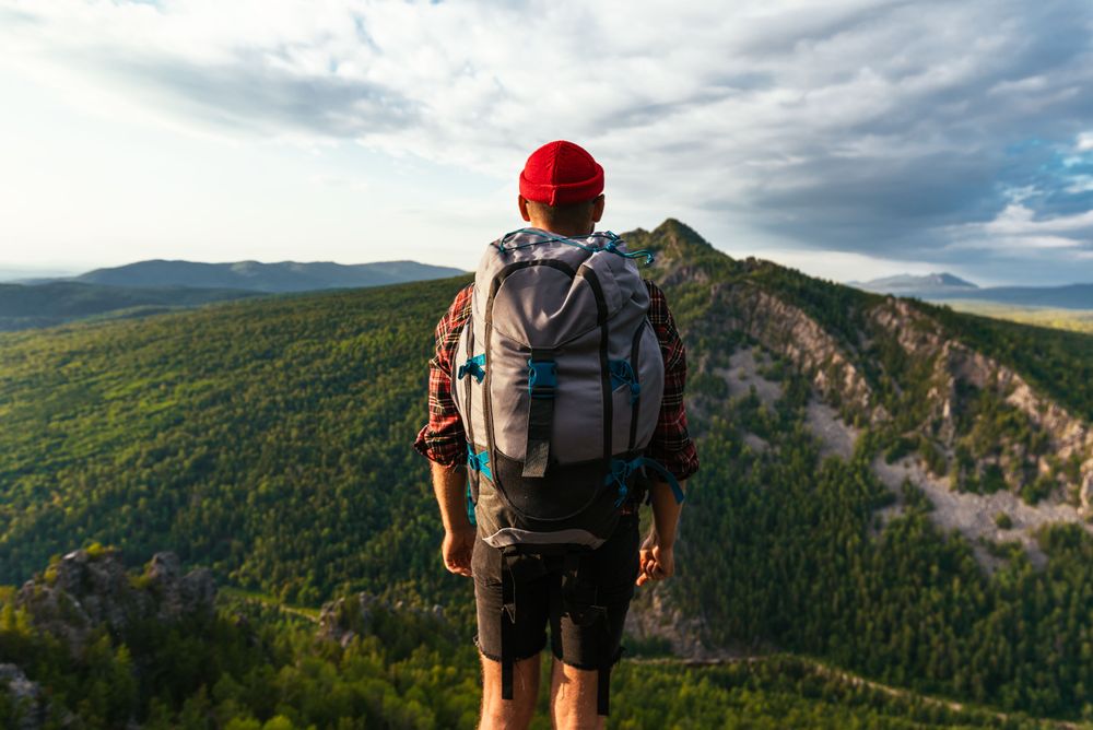 A tourist with a light backpack is standing on the top of the mountain because he knows how to pack light for a trip