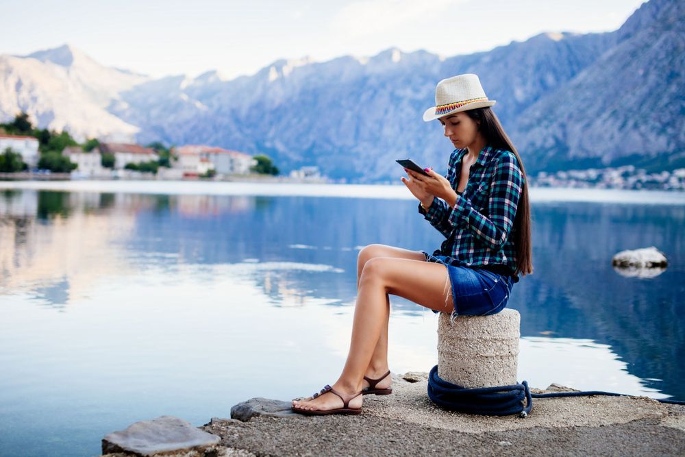 Woman looking at her mobile phone reading Top 10 Best Travel Apps to Consider in 2024