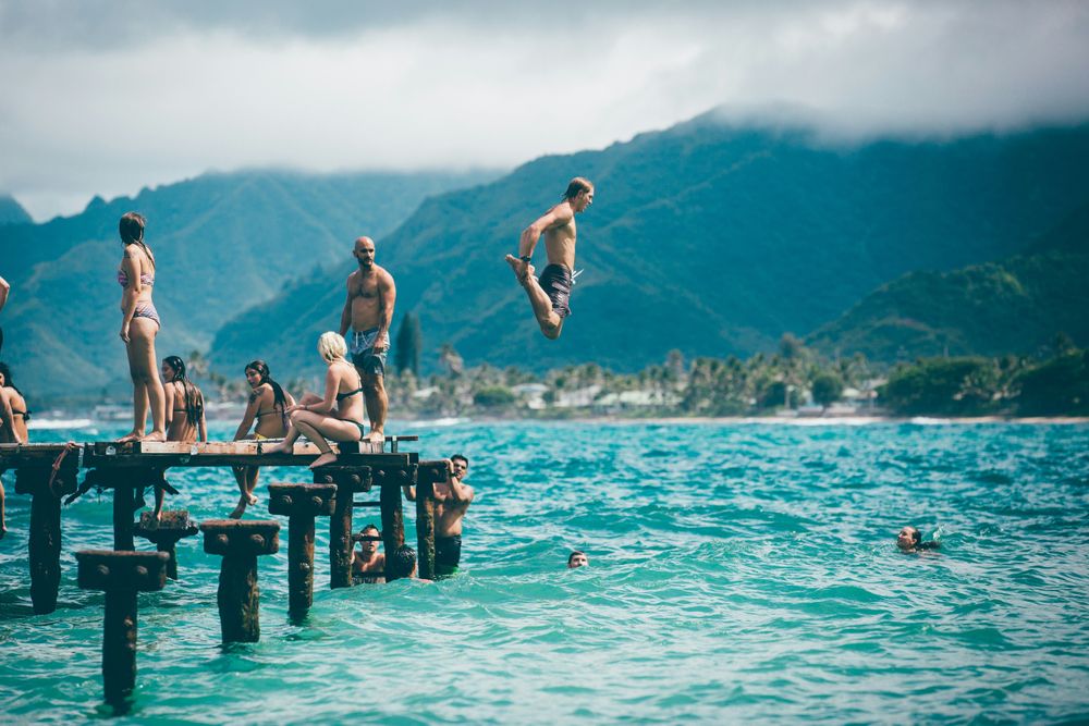 People on a peer, one man jumping in the water, representing the decision between solo travel or group travel