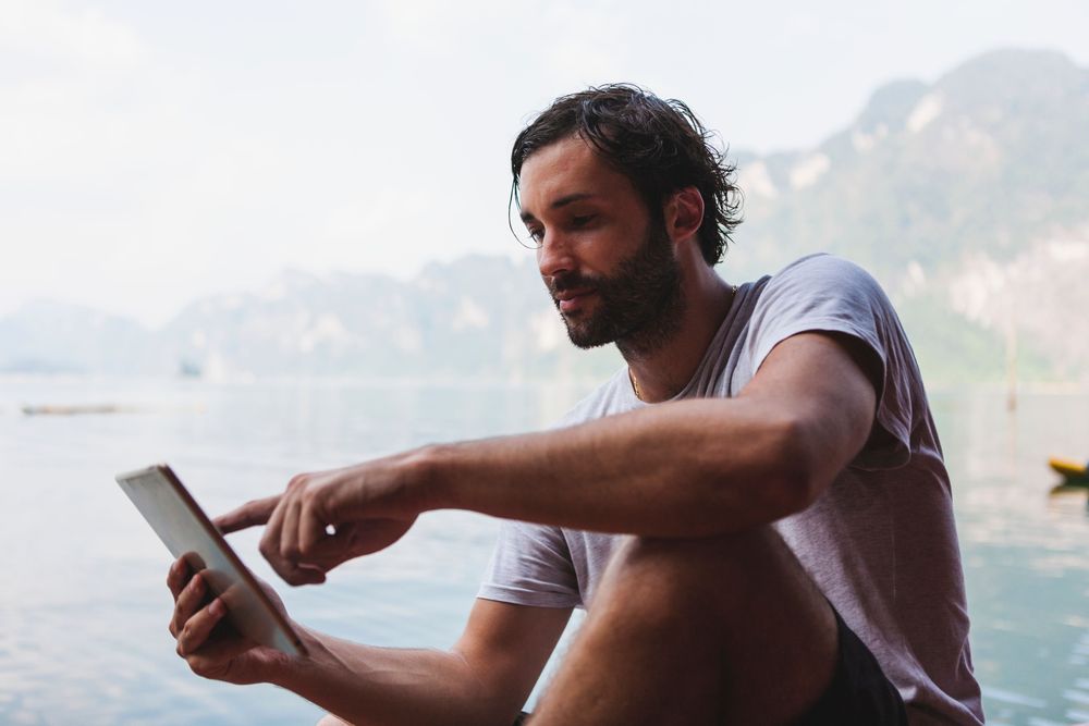  Men checking phone by the lake, mobile apps are part of our Travel Tips and Tricks