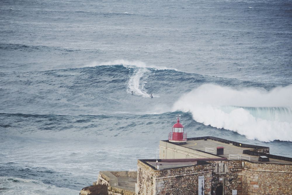 Surfer and lighthouse in Nazaré, Portugal, one of the Best Surfing Countries in Europe