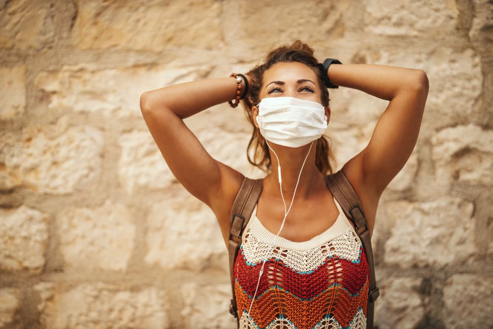 Mulher com máscara facial branca ficando segura enquanto viaja e representando como planejar uma viagem de última hora