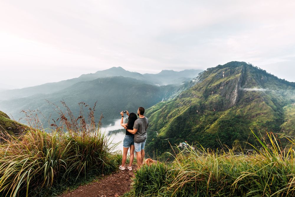 How to save money on flights, couple taking a photograph in the mountains