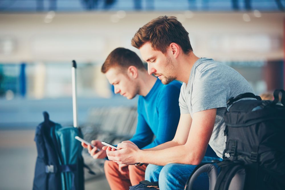 Two men sitting, looking at their phones and seeing a Travel Itinerary App