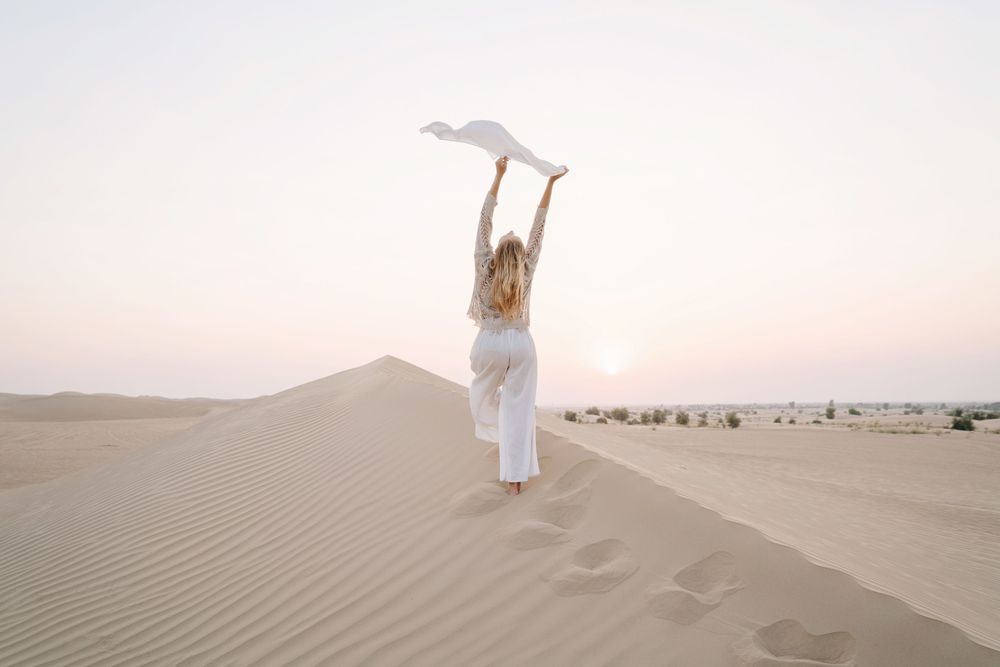 Woman holding a scarf in the sand, essential gear for solo female travel 